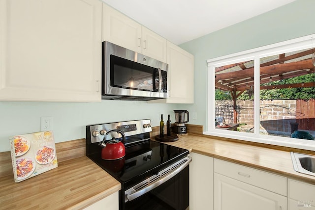 kitchen with stainless steel appliances, white cabinetry, and wood counters