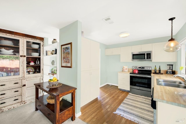 kitchen featuring sink, appliances with stainless steel finishes, light hardwood / wood-style floors, white cabinets, and decorative light fixtures