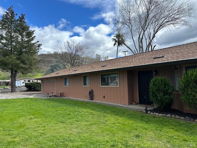 rear view of property with a garage, a shingled roof, and a lawn