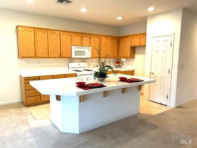 kitchen with white appliances, a breakfast bar area, light colored carpet, and a center island with sink