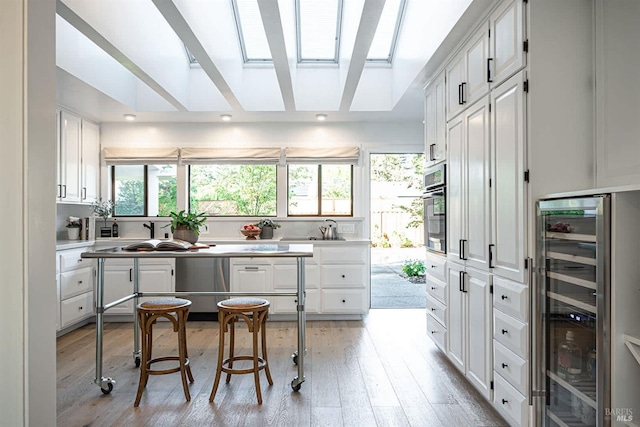 kitchen featuring wine cooler, white cabinetry, a skylight, and stainless steel oven