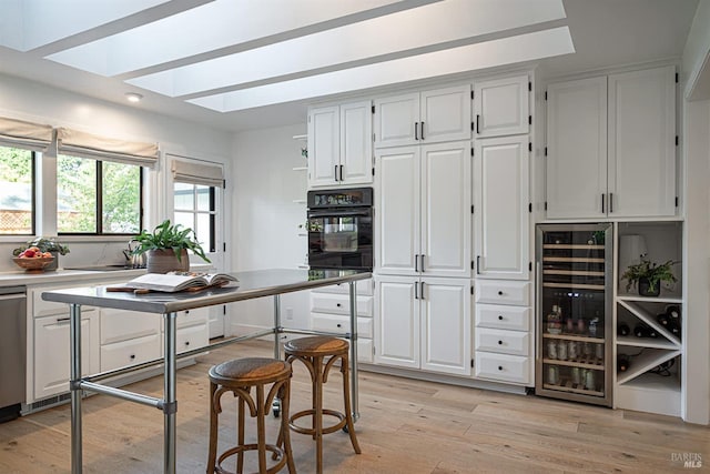 kitchen featuring wine cooler, a skylight, light wood-type flooring, black oven, and white cabinets