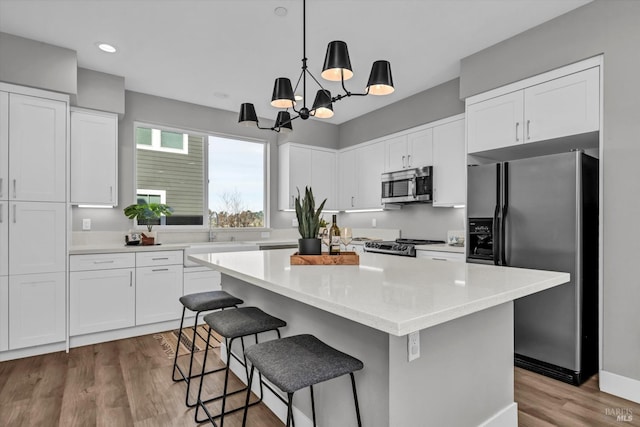 kitchen featuring a kitchen island, appliances with stainless steel finishes, sink, white cabinets, and hanging light fixtures