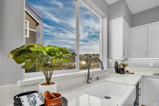 kitchen with white cabinetry, light stone countertops, and sink