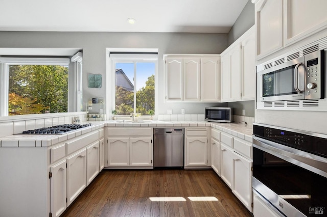 kitchen with stainless steel appliances, dark wood-type flooring, tile counters, and white cabinets