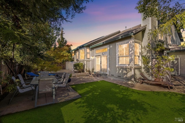 back house at dusk featuring a yard and a patio