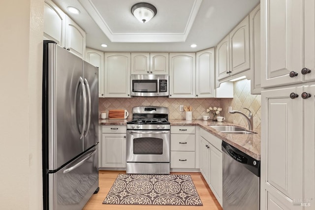 kitchen with stainless steel appliances, a raised ceiling, sink, and light wood-type flooring