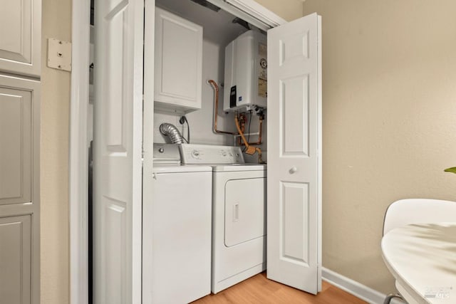 clothes washing area featuring cabinets, washer and clothes dryer, tankless water heater, and light hardwood / wood-style floors