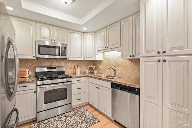 kitchen featuring light stone counters, sink, a raised ceiling, and appliances with stainless steel finishes