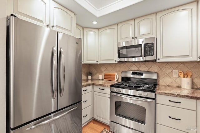 kitchen with appliances with stainless steel finishes, light hardwood / wood-style floors, and backsplash