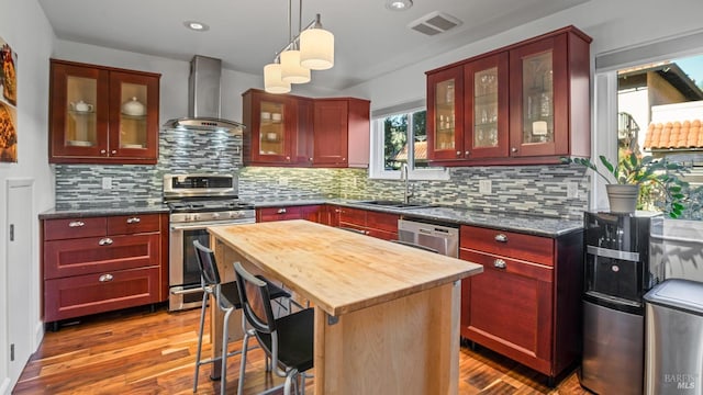 kitchen featuring wall chimney exhaust hood, sink, hanging light fixtures, a kitchen island, and stainless steel appliances