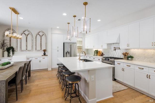 kitchen featuring high quality appliances, an island with sink, sink, hanging light fixtures, and custom range hood