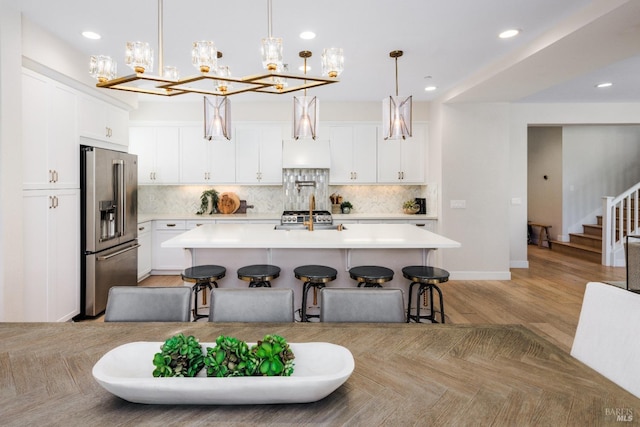 kitchen featuring appliances with stainless steel finishes, white cabinets, a kitchen bar, hanging light fixtures, and a kitchen island with sink