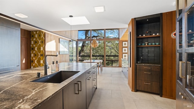 kitchen with sink, a skylight, light tile patterned floors, wooden walls, and pendant lighting