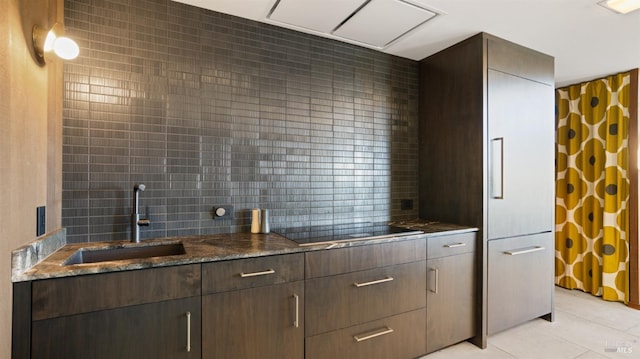 kitchen featuring light tile patterned flooring, sink, tasteful backsplash, dark stone countertops, and black electric cooktop