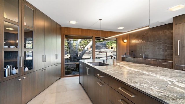 kitchen with sink, wood walls, decorative light fixtures, light tile patterned floors, and light stone countertops