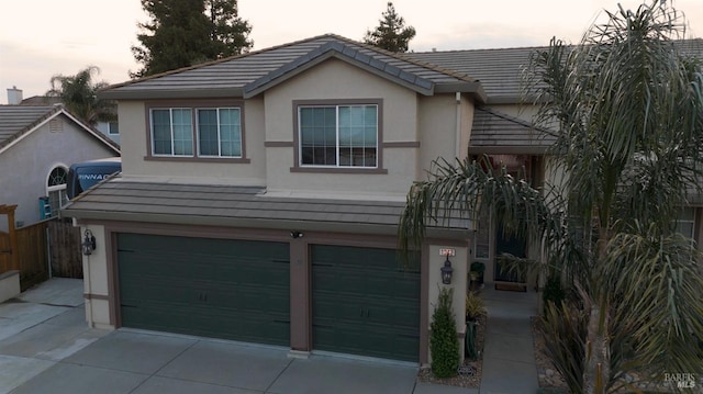 traditional home featuring concrete driveway, a tiled roof, an attached garage, and stucco siding