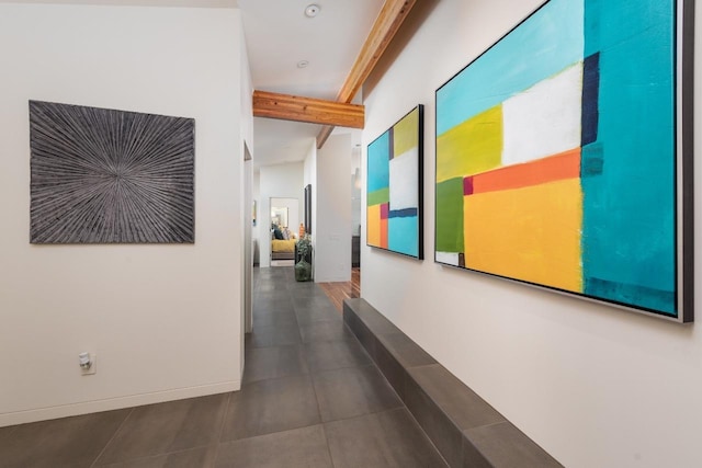 hall featuring dark tile patterned flooring, beamed ceiling, and baseboards