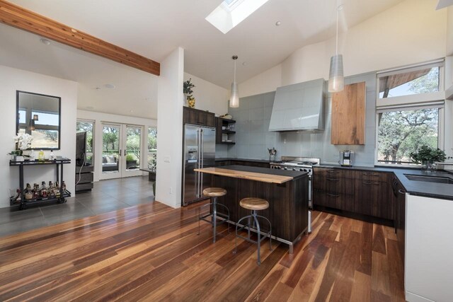 kitchen featuring high quality appliances, a sink, dark countertops, a skylight, and wall chimney exhaust hood