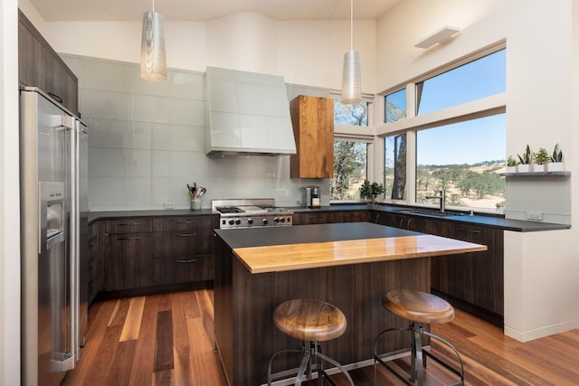 kitchen with wood finished floors, appliances with stainless steel finishes, a breakfast bar area, wooden counters, and custom exhaust hood