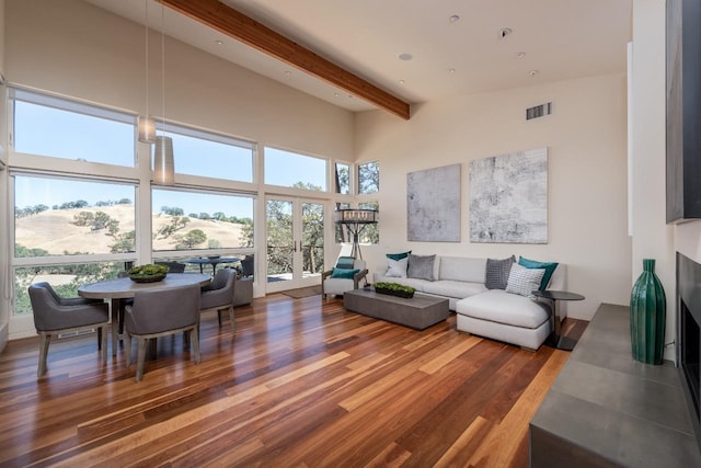 living area with visible vents, beam ceiling, a towering ceiling, and wood finished floors