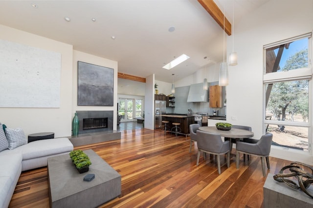 living room with beam ceiling, a tile fireplace, a skylight, wood finished floors, and high vaulted ceiling