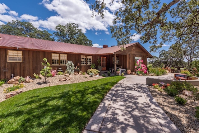 ranch-style home with a chimney, board and batten siding, metal roof, and a front lawn