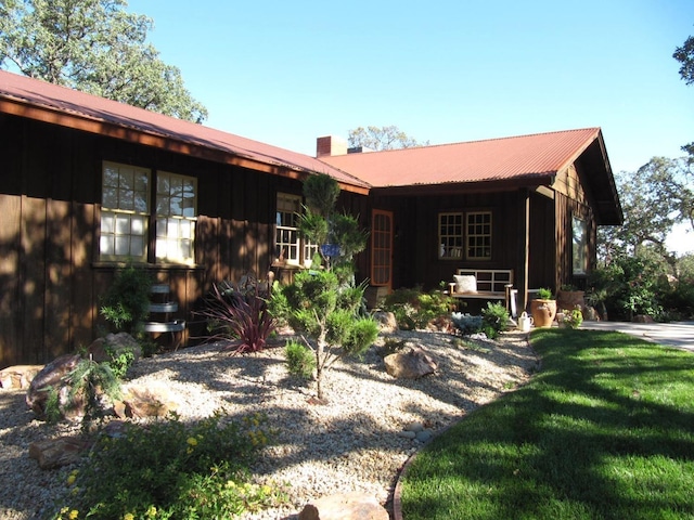 view of front of property with board and batten siding, a chimney, a front yard, and metal roof