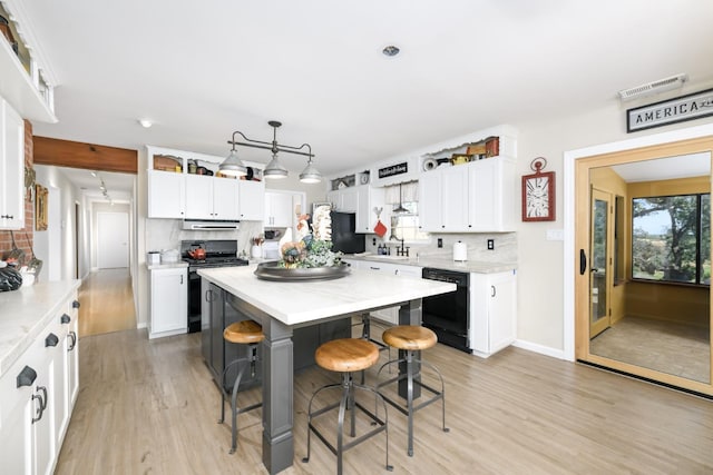 kitchen with light wood-style floors, a kitchen bar, black appliances, and white cabinets