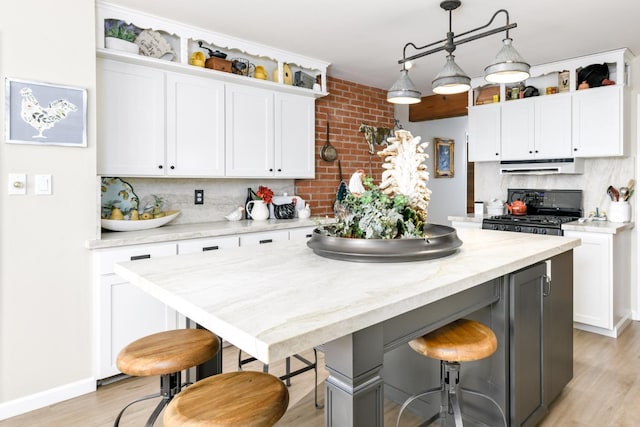 kitchen featuring black range with gas cooktop, light wood-style flooring, tasteful backsplash, a breakfast bar, and white cabinets