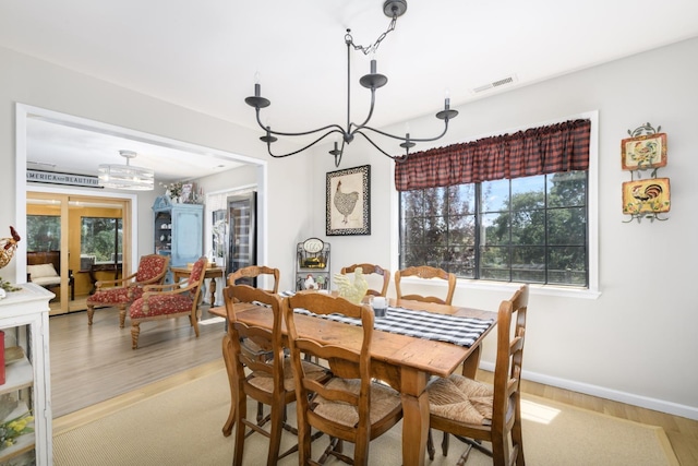 dining space with baseboards, a notable chandelier, visible vents, and light wood-style floors