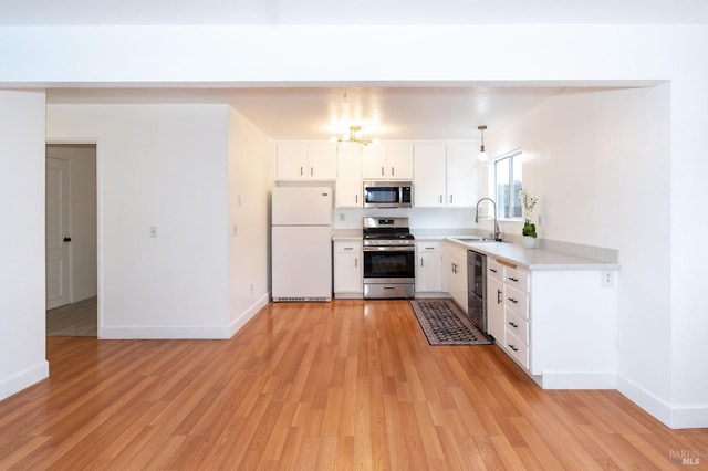 kitchen with appliances with stainless steel finishes, white cabinetry, sink, hanging light fixtures, and light hardwood / wood-style floors