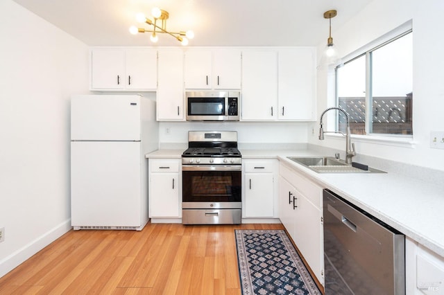 kitchen featuring decorative light fixtures, white cabinetry, sink, stainless steel appliances, and light wood-type flooring