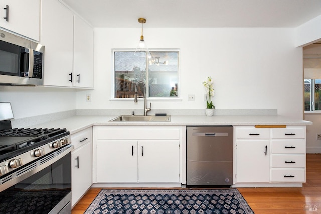 kitchen featuring pendant lighting, sink, appliances with stainless steel finishes, white cabinetry, and light wood-type flooring