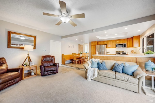 living room featuring sink, light carpet, a textured ceiling, a tray ceiling, and ceiling fan