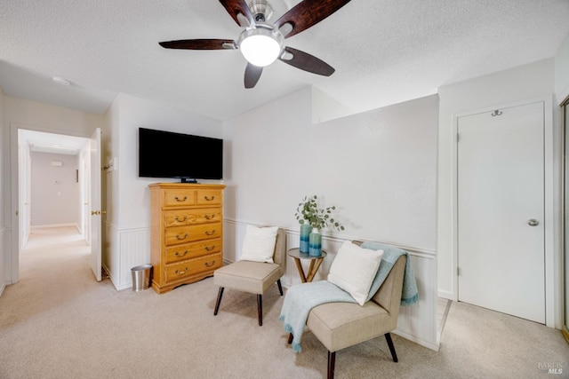 sitting room featuring ceiling fan, light colored carpet, and a textured ceiling