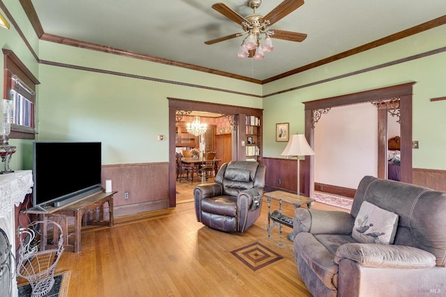 living room with ceiling fan with notable chandelier, ornamental molding, wood walls, and light wood-type flooring