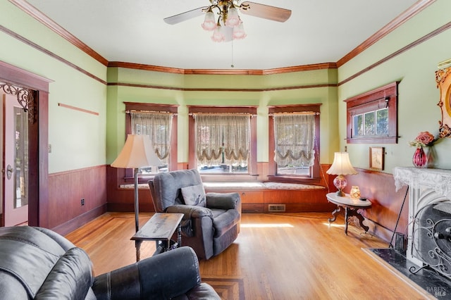 living room featuring ornamental molding, light hardwood / wood-style floors, wooden walls, and ceiling fan