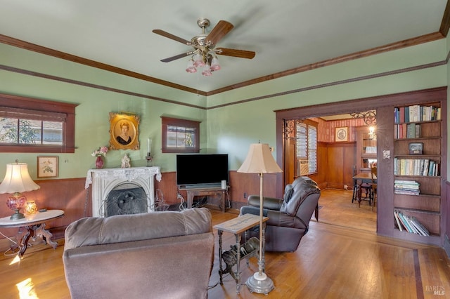 living room with crown molding, ceiling fan, wooden walls, and light hardwood / wood-style flooring