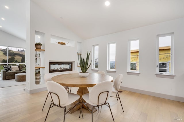 dining area with a multi sided fireplace, high vaulted ceiling, and light hardwood / wood-style floors