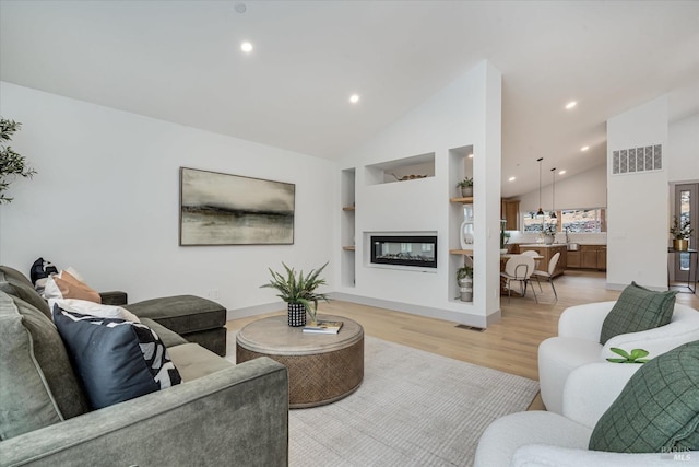 living room with lofted ceiling, built in shelves, and light hardwood / wood-style floors