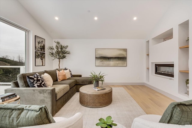 living room with vaulted ceiling, built in features, and light wood-type flooring