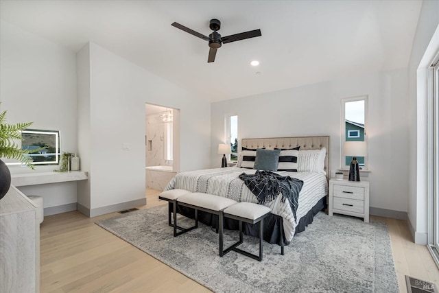 bedroom with ensuite bathroom, vaulted ceiling, ceiling fan, light hardwood / wood-style floors, and multiple windows