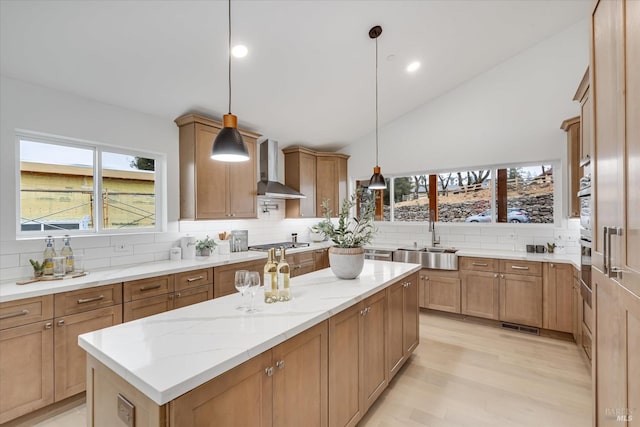 kitchen with sink, decorative light fixtures, a center island, decorative backsplash, and wall chimney range hood