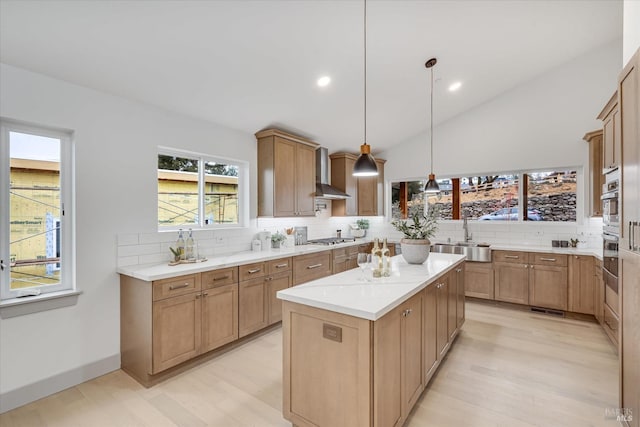 kitchen with sink, hanging light fixtures, a kitchen island, stainless steel gas stovetop, and wall chimney range hood