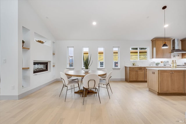 dining room with vaulted ceiling, a healthy amount of sunlight, built in features, and light hardwood / wood-style floors