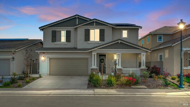 craftsman-style home featuring solar panels, stucco siding, covered porch, concrete driveway, and an attached garage