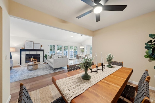 dining room featuring hardwood / wood-style flooring, ceiling fan, lofted ceiling, and a tile fireplace