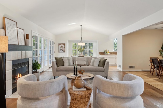 living room with light hardwood / wood-style floors, a tiled fireplace, and vaulted ceiling