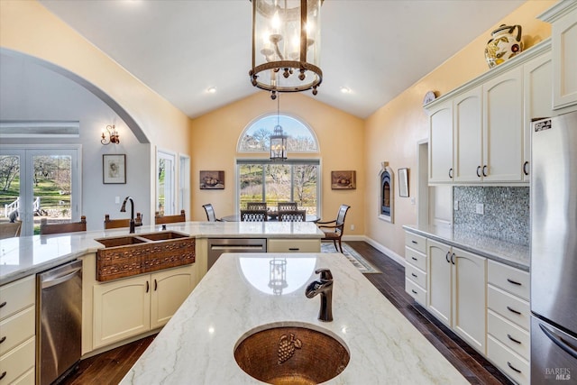 kitchen featuring lofted ceiling, sink, appliances with stainless steel finishes, pendant lighting, and light stone countertops